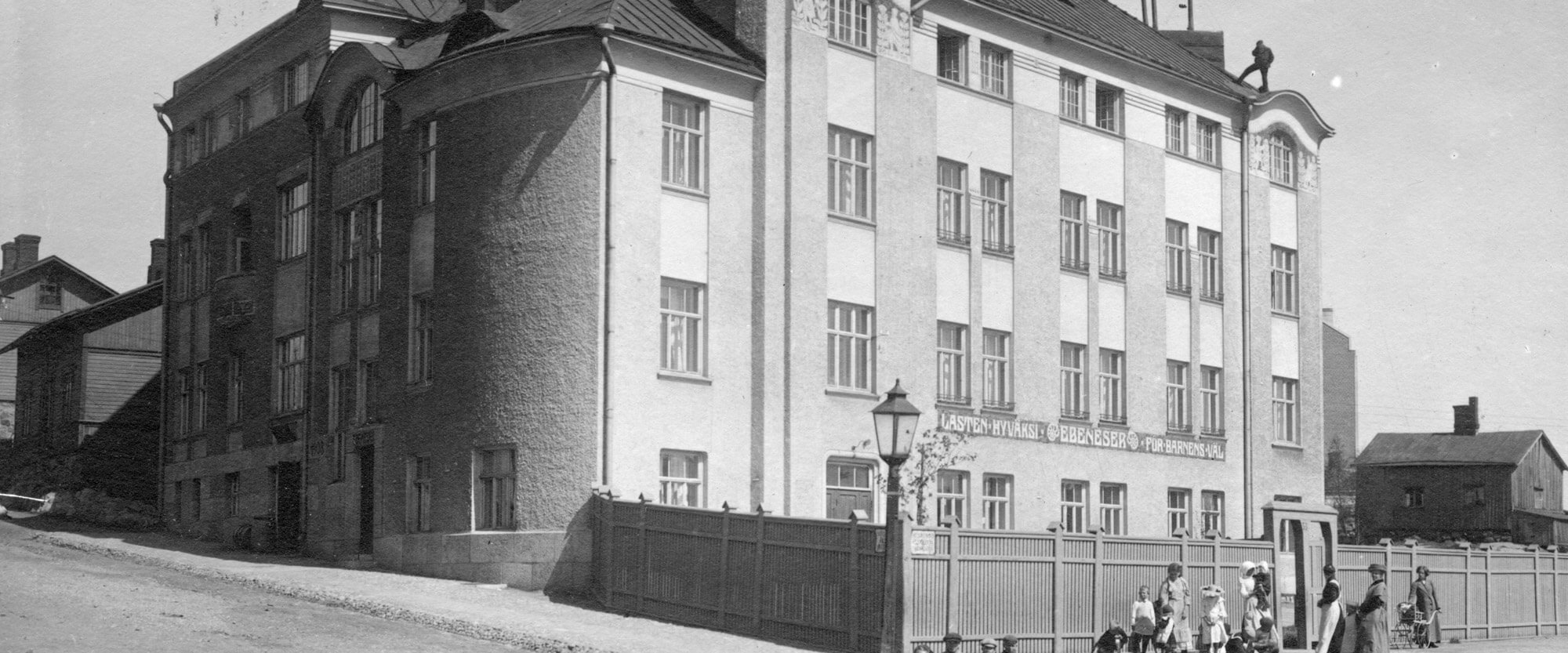 Mustavalkokuva Ebeneser-talosta 1910-luvulla. Kuva otettu viistosti Helsinginkadun ja Harjukadun risteyksestä paljastaen Ebeneser-talon julkisivun kahdelta puolelta. Lastentarhamuseon valokuvakokoelma.