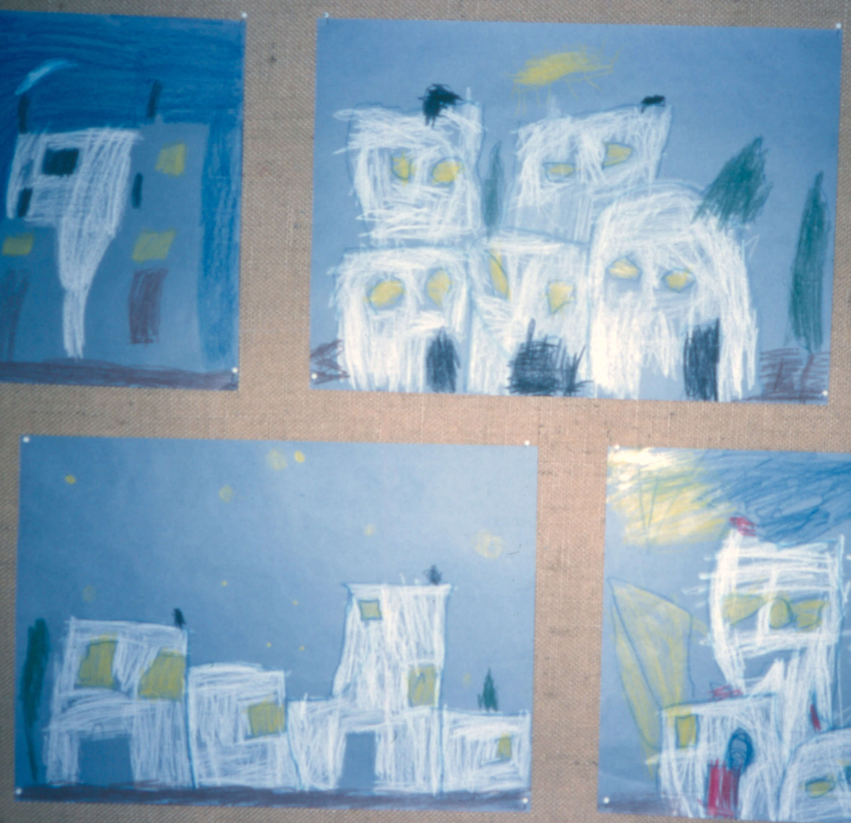 Lasten sinipohjaiselle paperille valkoisella ja tummansinisellä liidulla piirtämiä tasakattoisia taloja. Lastentarhamuseon valokuvakokolema.