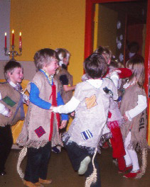 Kuvassa lapsia tanssii piirissä pukeutuneina ilmeisesti peikoiksi tai muiksi säkkikangasvaatetuksen omaavaksi maahiaiseksi. Lastentarhamuseon valokuvakokoelma.