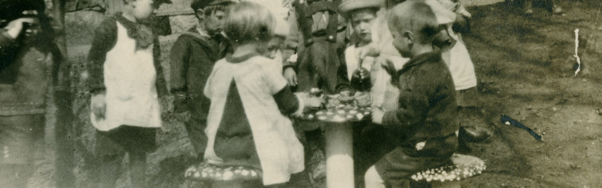 Lapsia leikkimässä kotileikkiä Ebeneserin pihalla leikkimökin edessä olevilla kärpässienituoleilla, 1925-1927. Lsatentarhamuseon valokuvakokoelma.