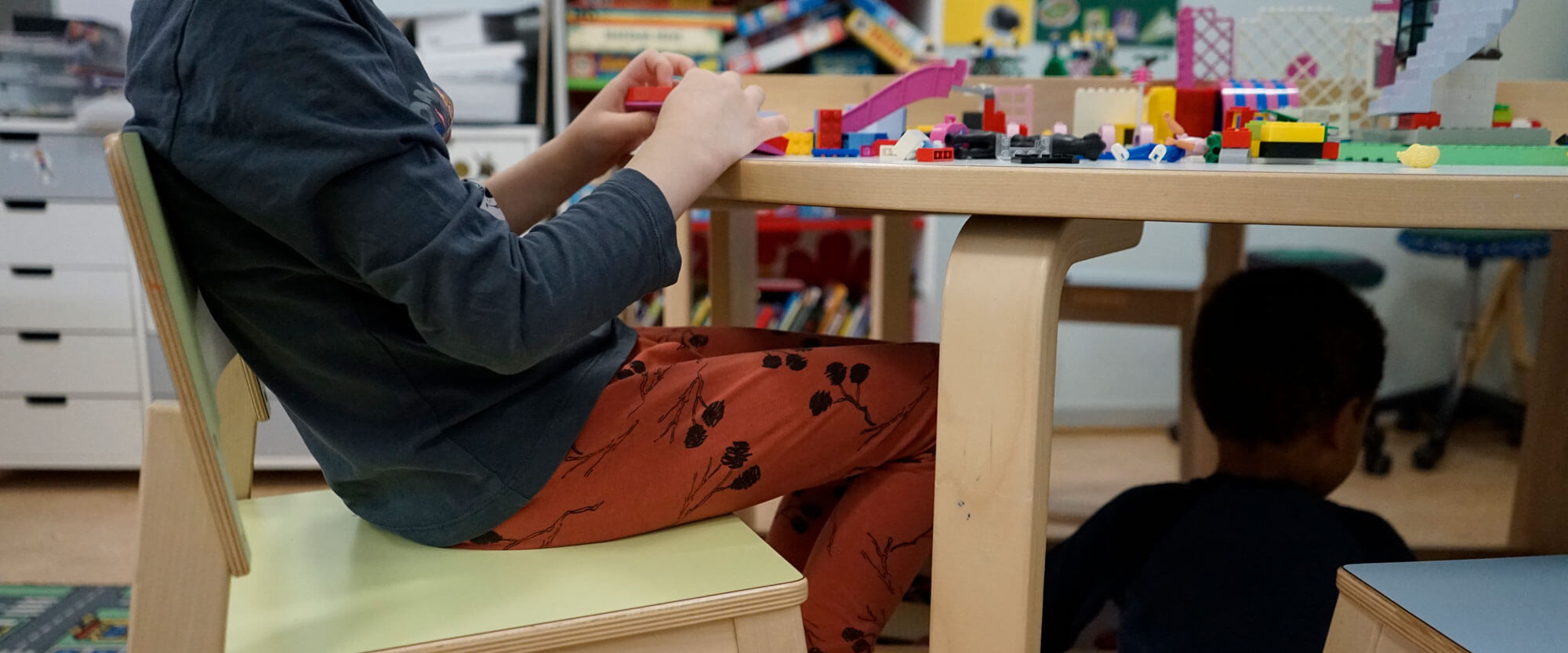 Kuvassa kaksi poikaa leikkii ja rakentelee legoilla päiväkoti Ebeneserin eräässä ryhmätilassa. Toinen pojista on mennyt leikkimään pöydän alle. Kuvaaja: Sanna Kämäräinen