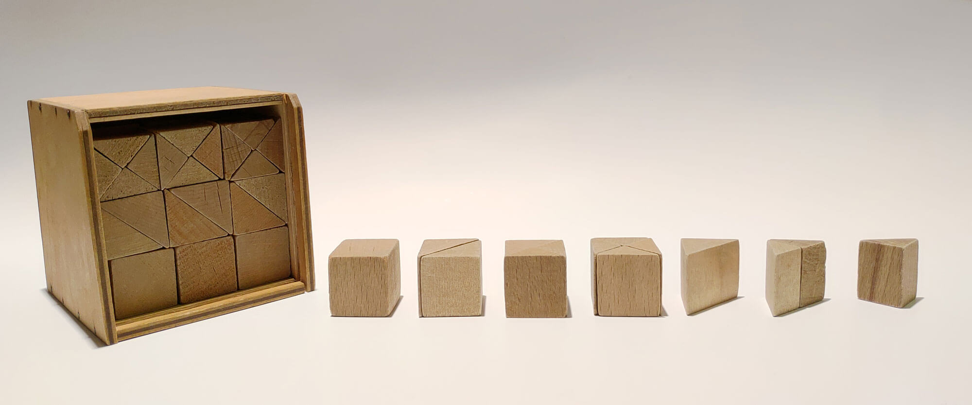 Kuvassa vasemmalla on puinen kuution muotoinen laatikko, jonka etuseinä on poistettu ja sen sisältä paljastuu pieniä puisia palikoita. Palikkakokonaisuus on aktiivisuuspedagogi Friedrich Fröbelin suunnittelema palikkakokonaisuus, jonka hän nimesi viidenneksi lahjaksi. Puisen kuutiolaatikon vieressä on rivissä puisia palikoita: kuutioita sekä särmiöitä, jotka muodostavat kuution.