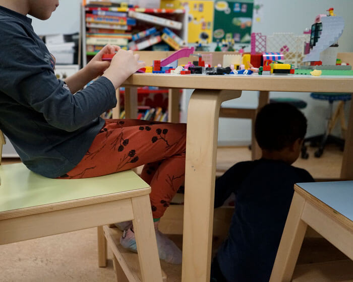 Kuvassa kaksi poikaa leikkii ja rakentelee legoilla päiväkoti Ebeneserin eräässä ryhmätilassa. Toinen pojista on mennyt leikkimään pöydän alle. Kuvaaja: Sanna Kämäräinen