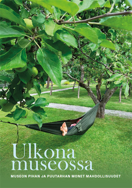Ulkona museossa – Museon pihan ja puutarhan monet mahdollisuudet -julkaisun kannessa vehreässä puutarhassa makoilee henkilö vihreässä riippukeinussa jalat vain pilkistäen.